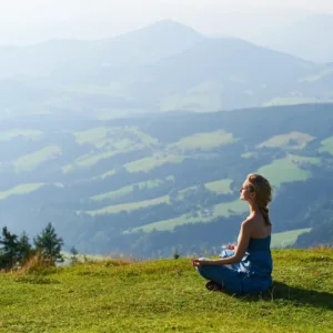 Person meditiert auf einer Wiese mit Blick auf die Berge