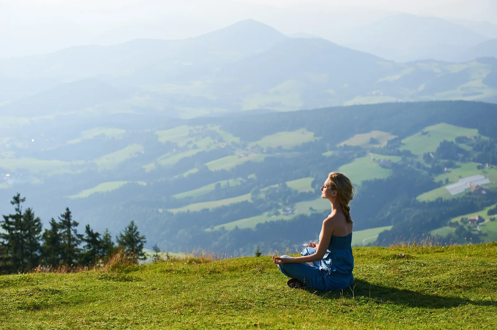 Person meditiert auf einer Wiese mit Blick auf die Berge