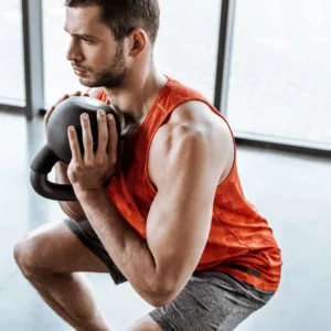 Mann in der Kniebeuge mit Kettlebell vor einer Fensterfront