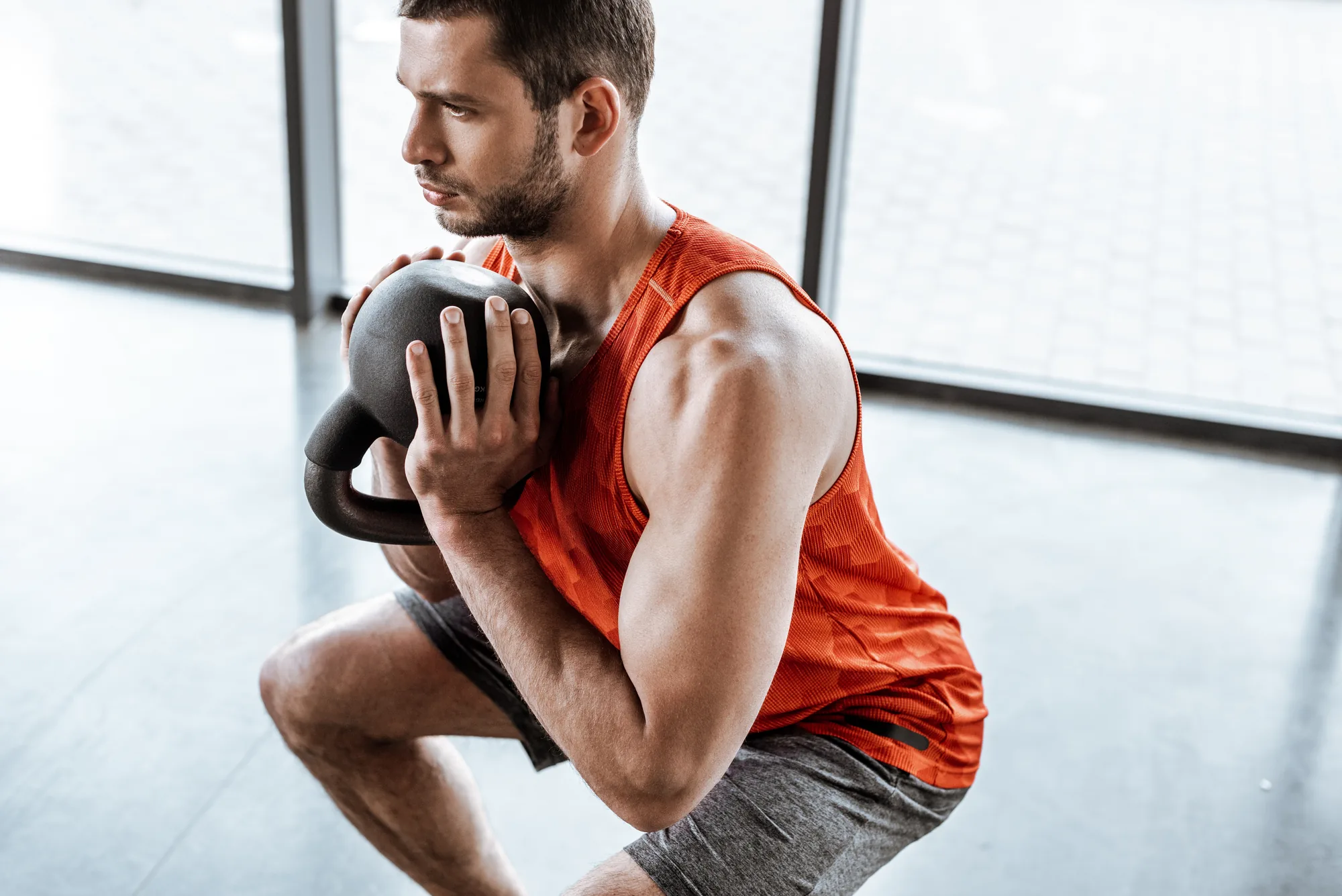 Mann in der Kniebeuge mit Kettlebell vor einer Fensterfront