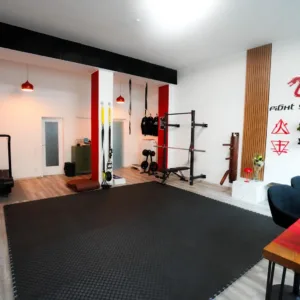 Trainingsflaeche im Studio Lehel mit Matte, Kraftgeraeten und dem Fight Yourself Logo an der Wand